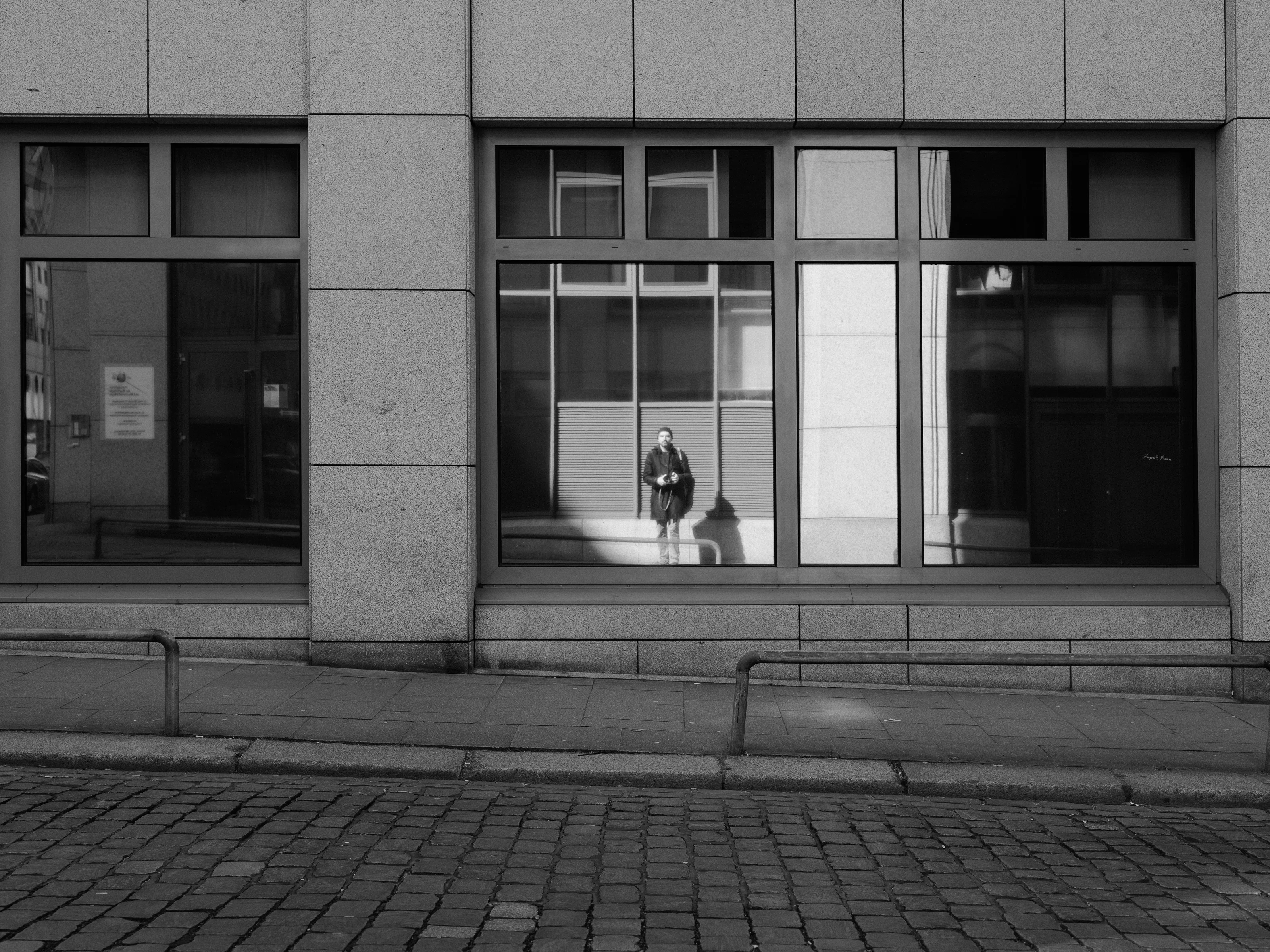 Person reflected in building window on a city street.