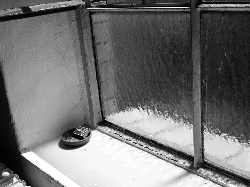 A small round tray with an empty cigarette box on a windowsill next to frosted glass windows.