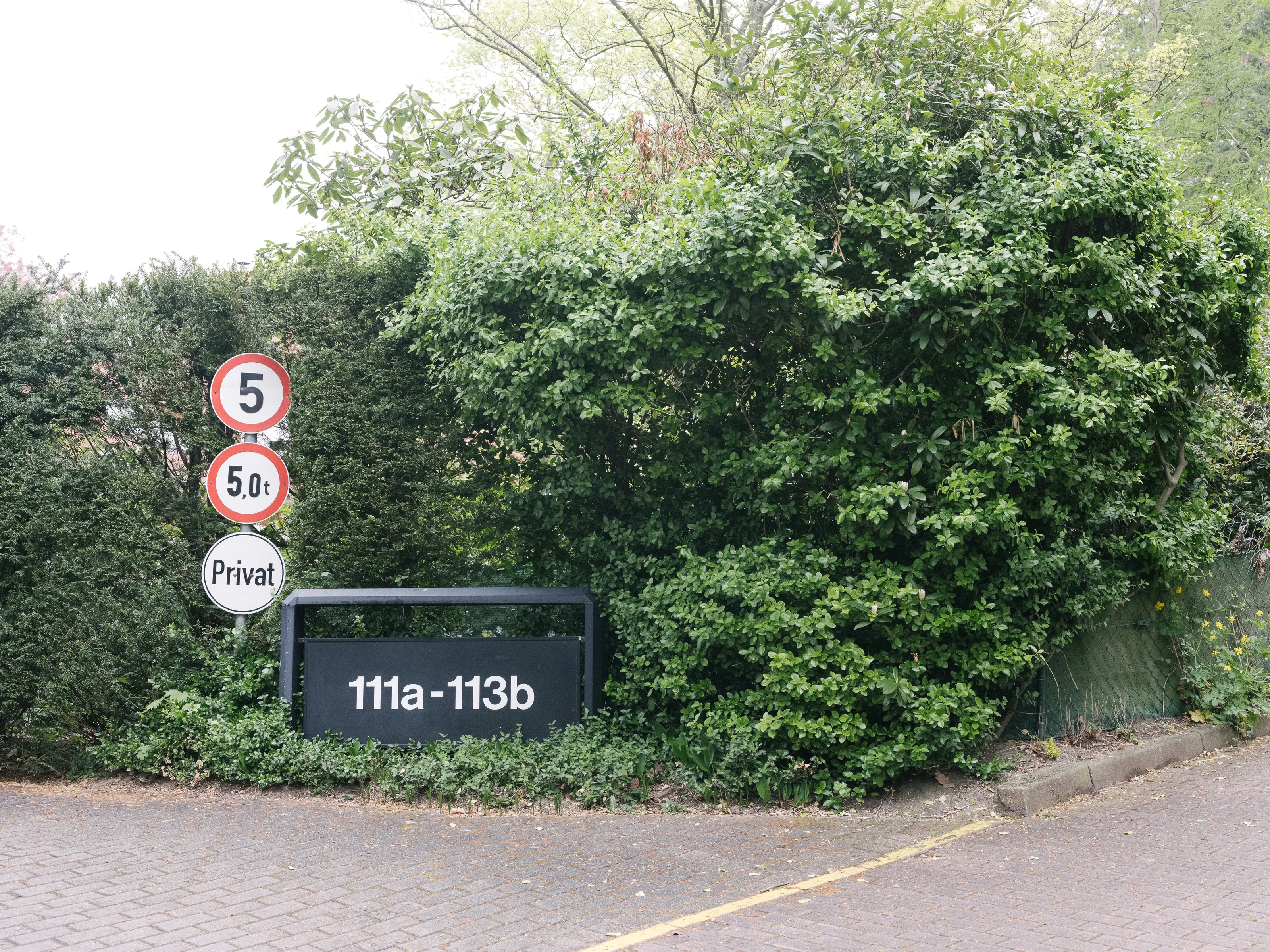 Safety signs and a location sign are placed beside dense greenery.