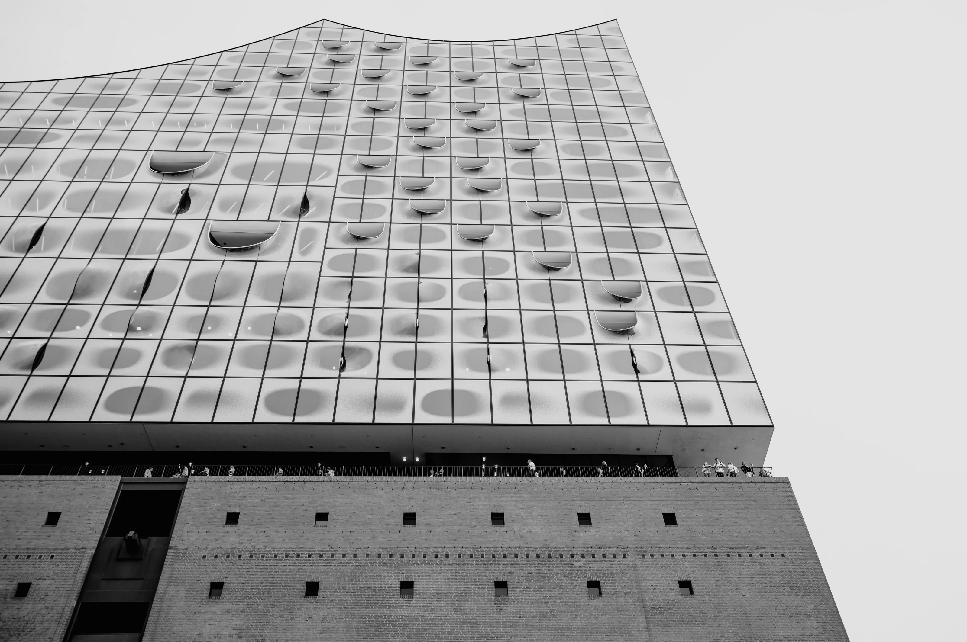 Black and white photo of a modern building facade with a wavy glass structure and brick base.