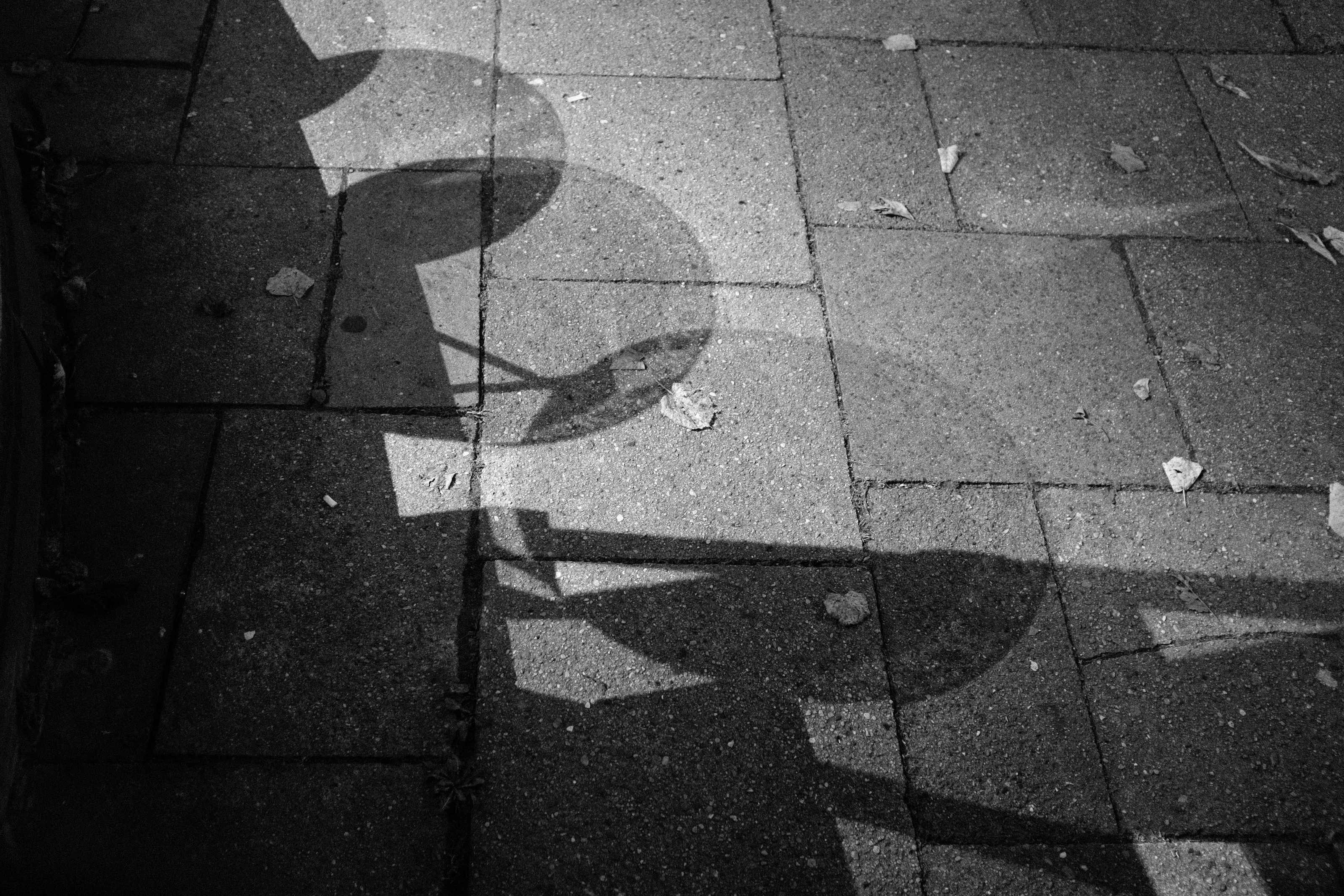Shadows of circular stools cast on a paved sidewalk.