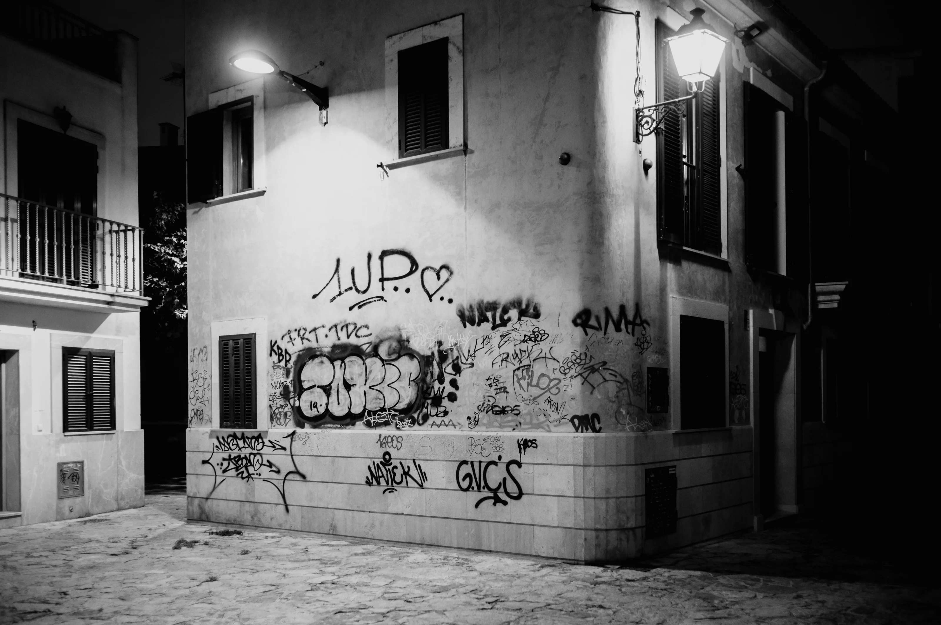 Black and white photo of a graffiti-covered building corner illuminated by streetlights.