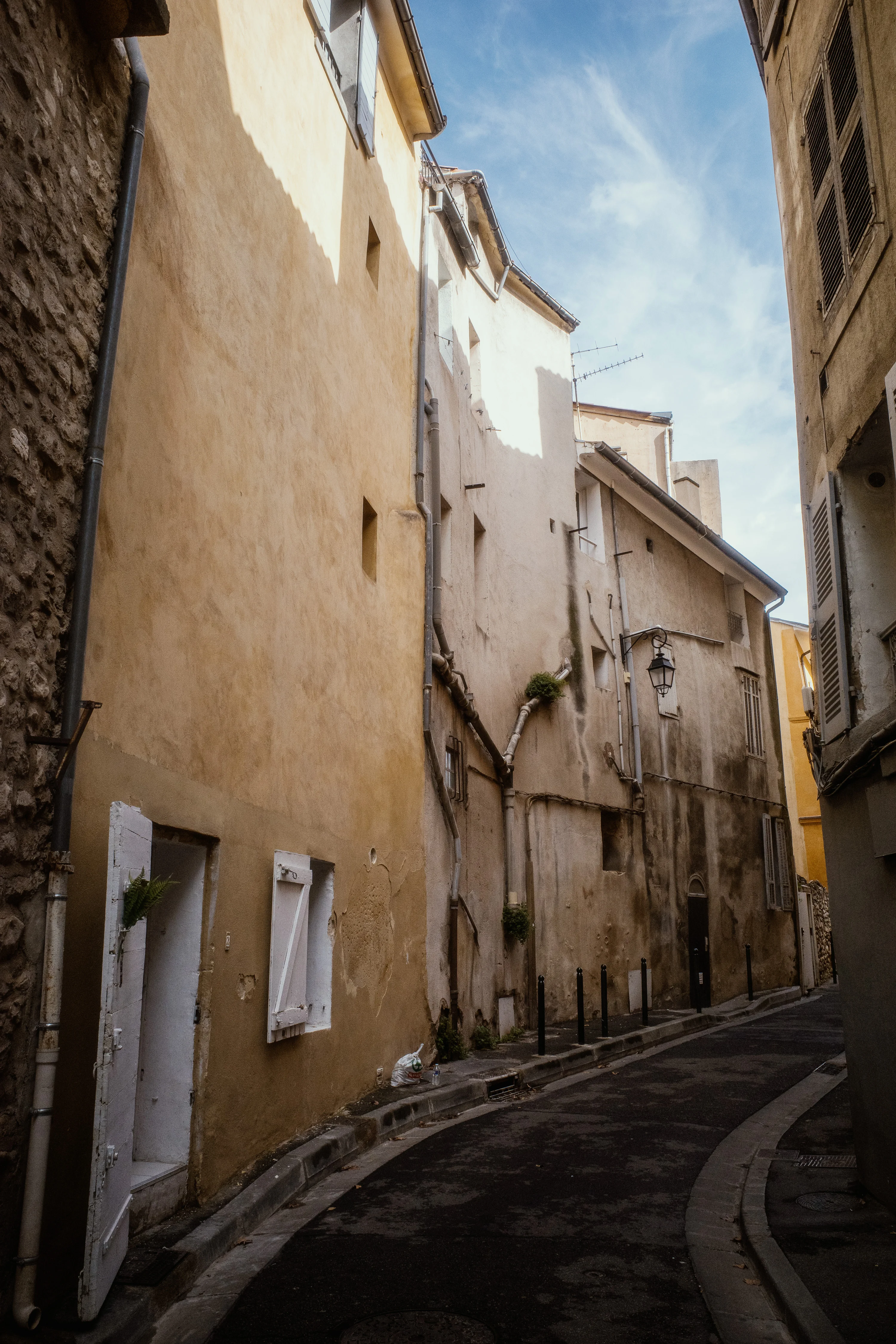 Narrow alleyway with tall, aged buildings under a blue sky.