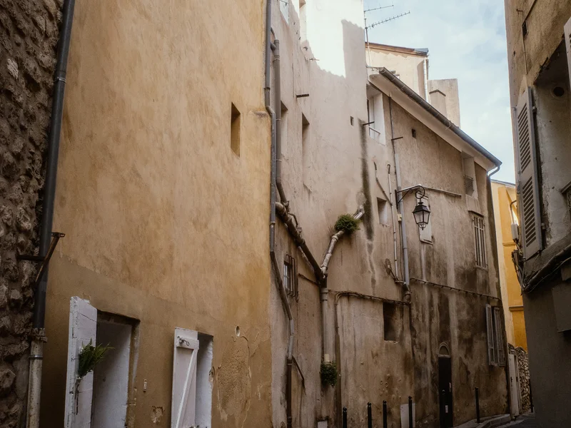 Narrow alleyway with tall, aged buildings under a blue sky.