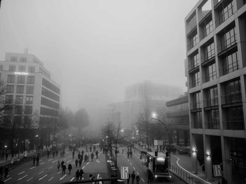 Black and white photo of a busy city street with people walking and buildings shrouded in fog.