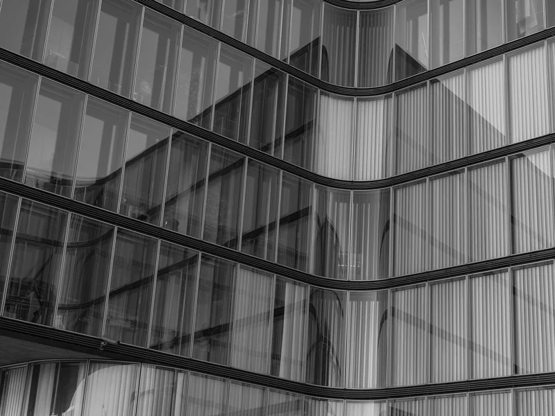 Black and white architectural shot of a modern glass building with reflections.