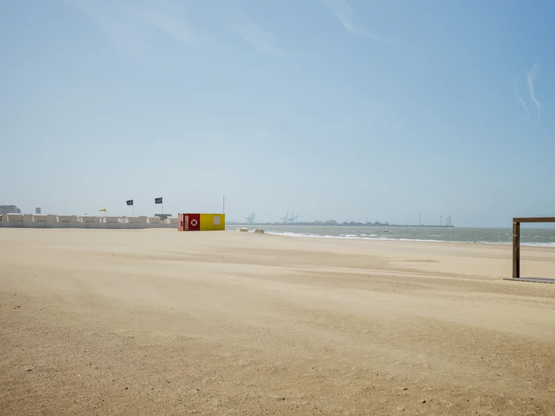 A sandy beach with a lifeguard station and a wooden frame overlooking the sea, under a clear blue sky.