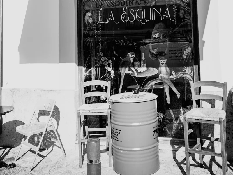 Black and white photo of a cafe entrance with chairs and a barrel outside.