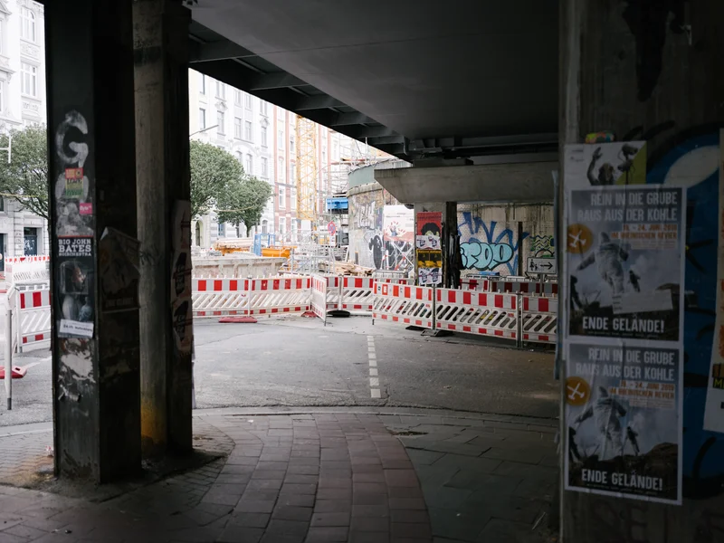 Urban scene under a bridge with construction barriers and graffiti-covered columns.
