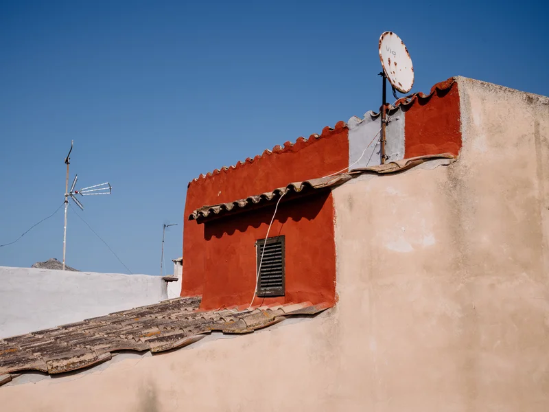 Rustic red-tiled rooftop with satellite dish against a clear blue sky.