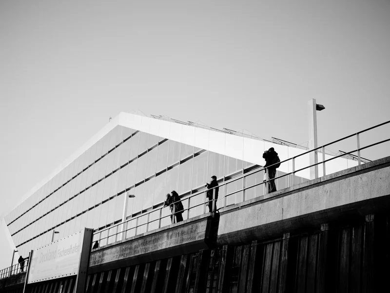 People standing on a walkway in front of a modern, angular building.