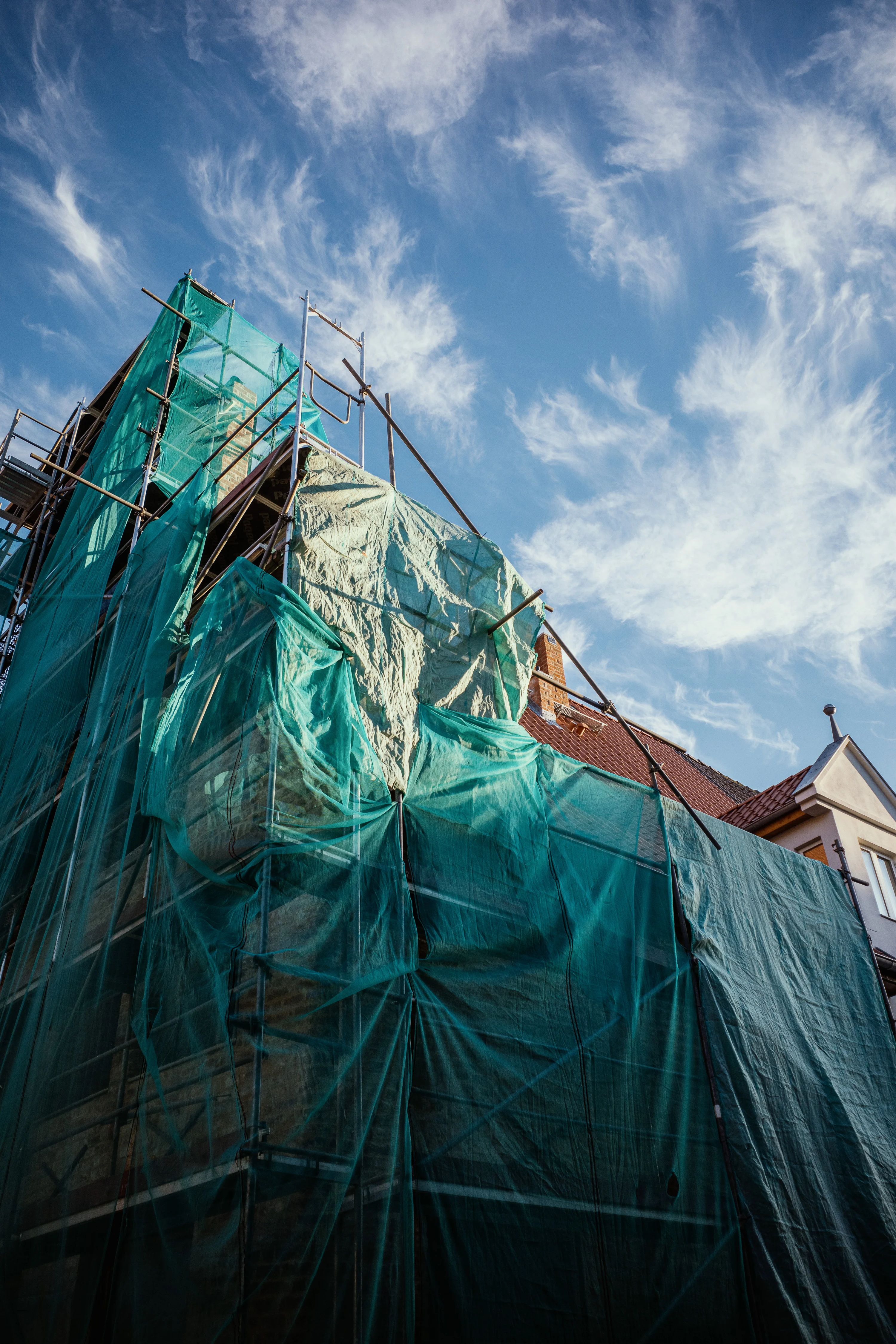 Building under construction covered with green netting against a blue sky with wispy clouds.