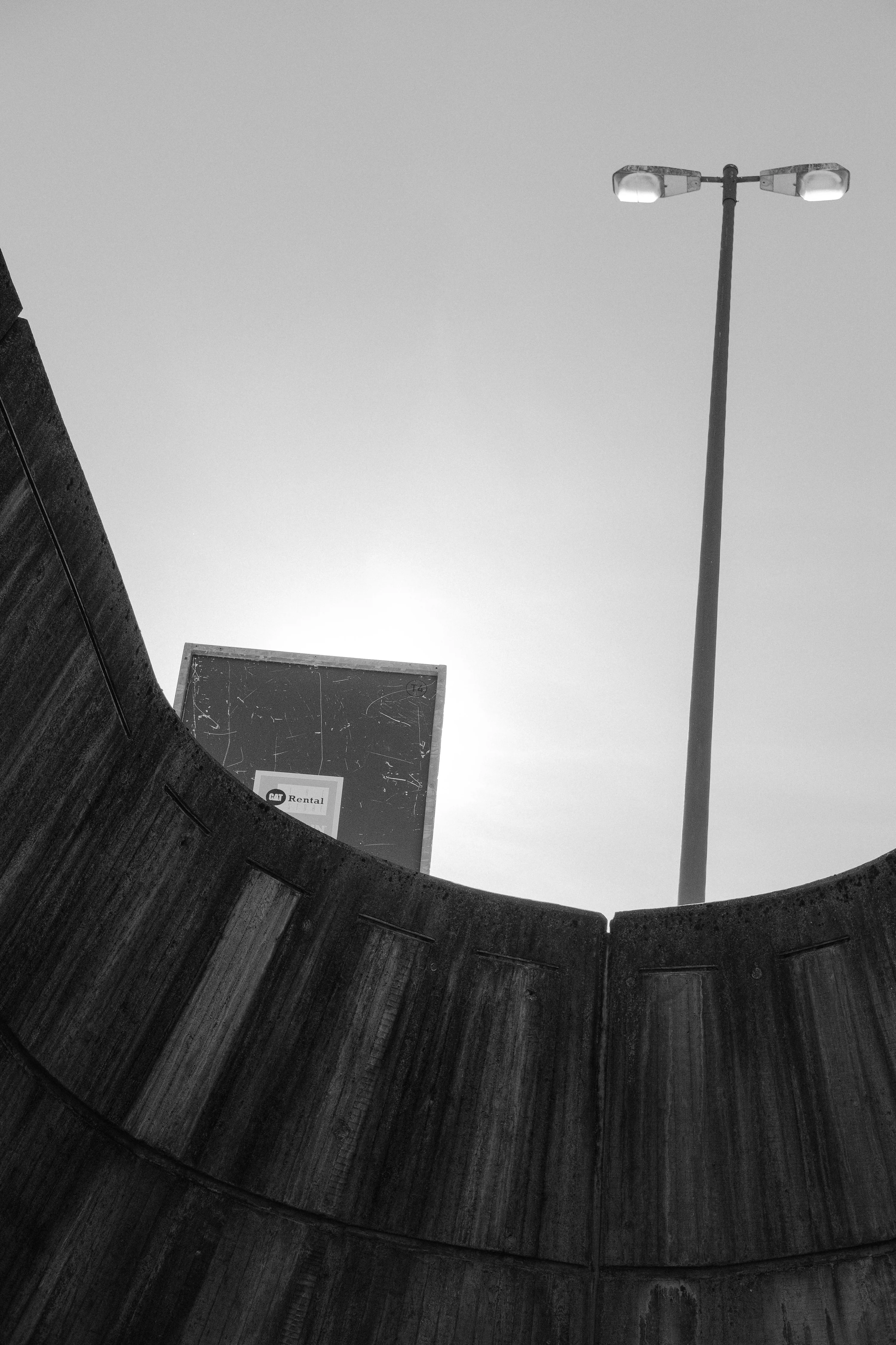A street light and a billboard partially obscured by a curved concrete wall under a clear sky.