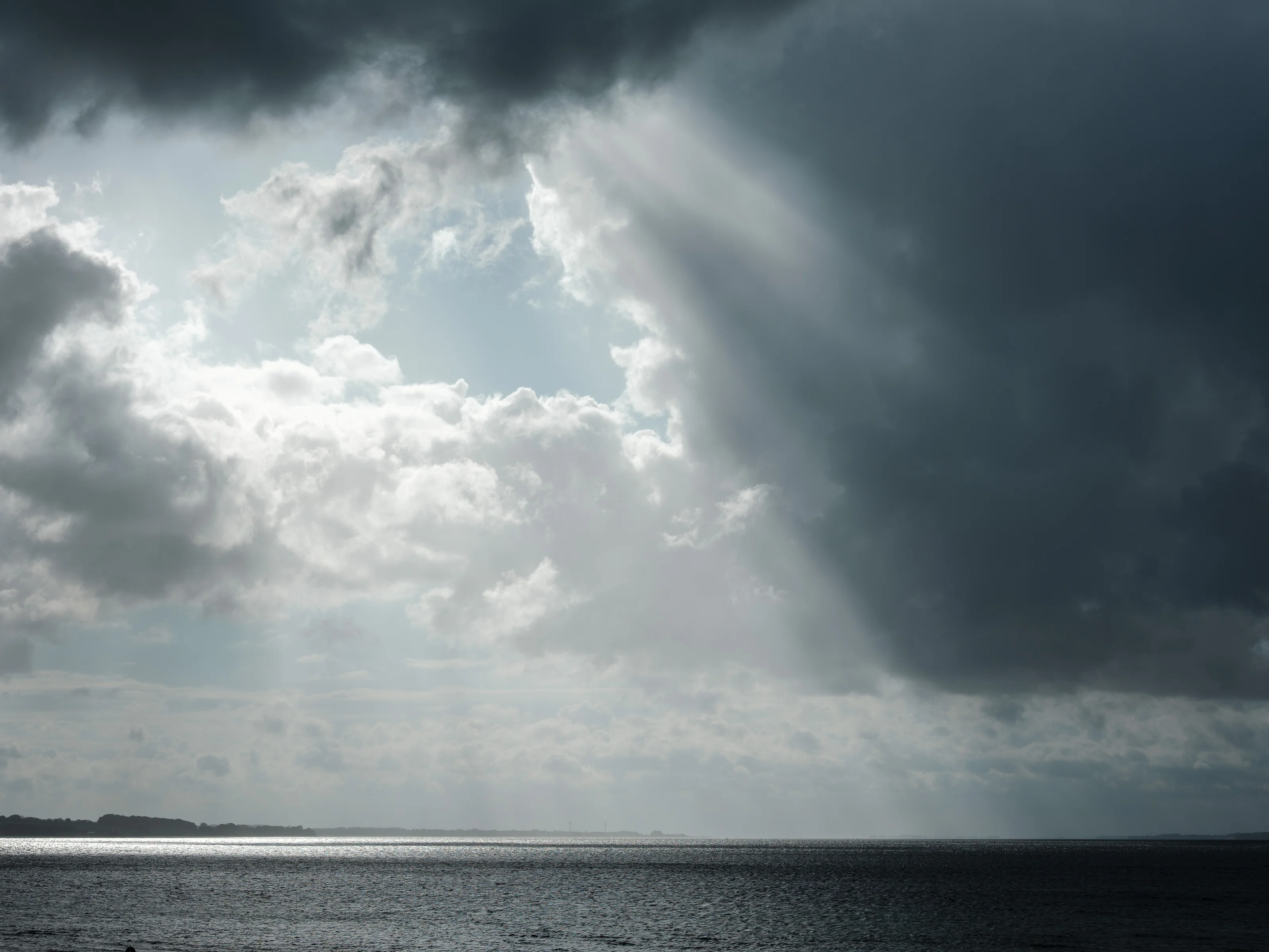 Sun rays breaking through dark clouds over a calm sea.