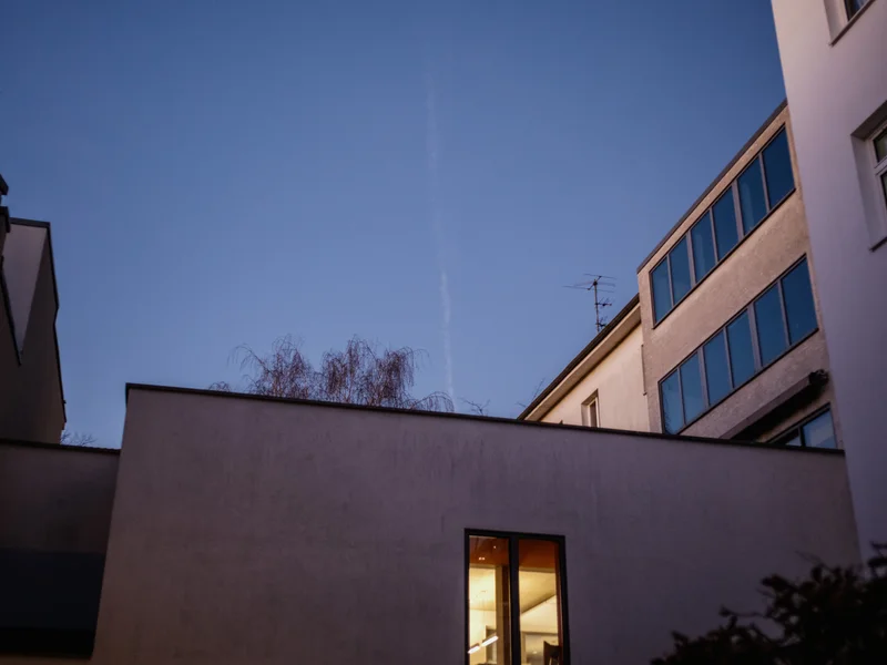 Evening view of a building courtyard with a lit window against a clear sky.