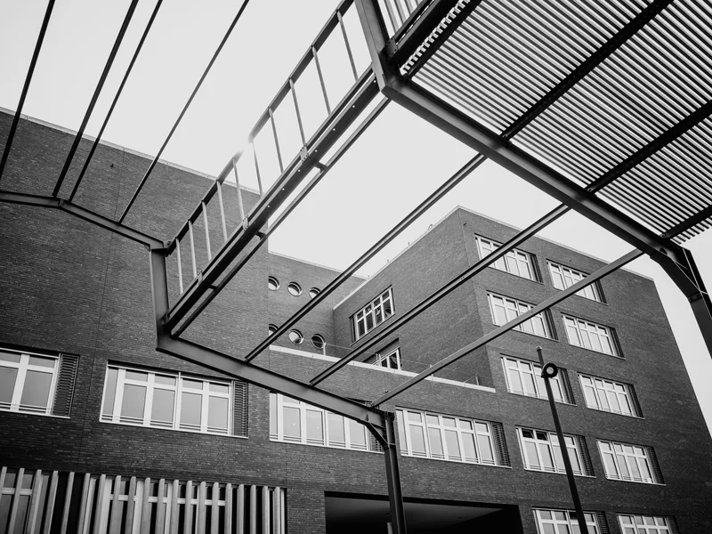 Black and white photograph of a modern brick building with geometric metal frames overhead.