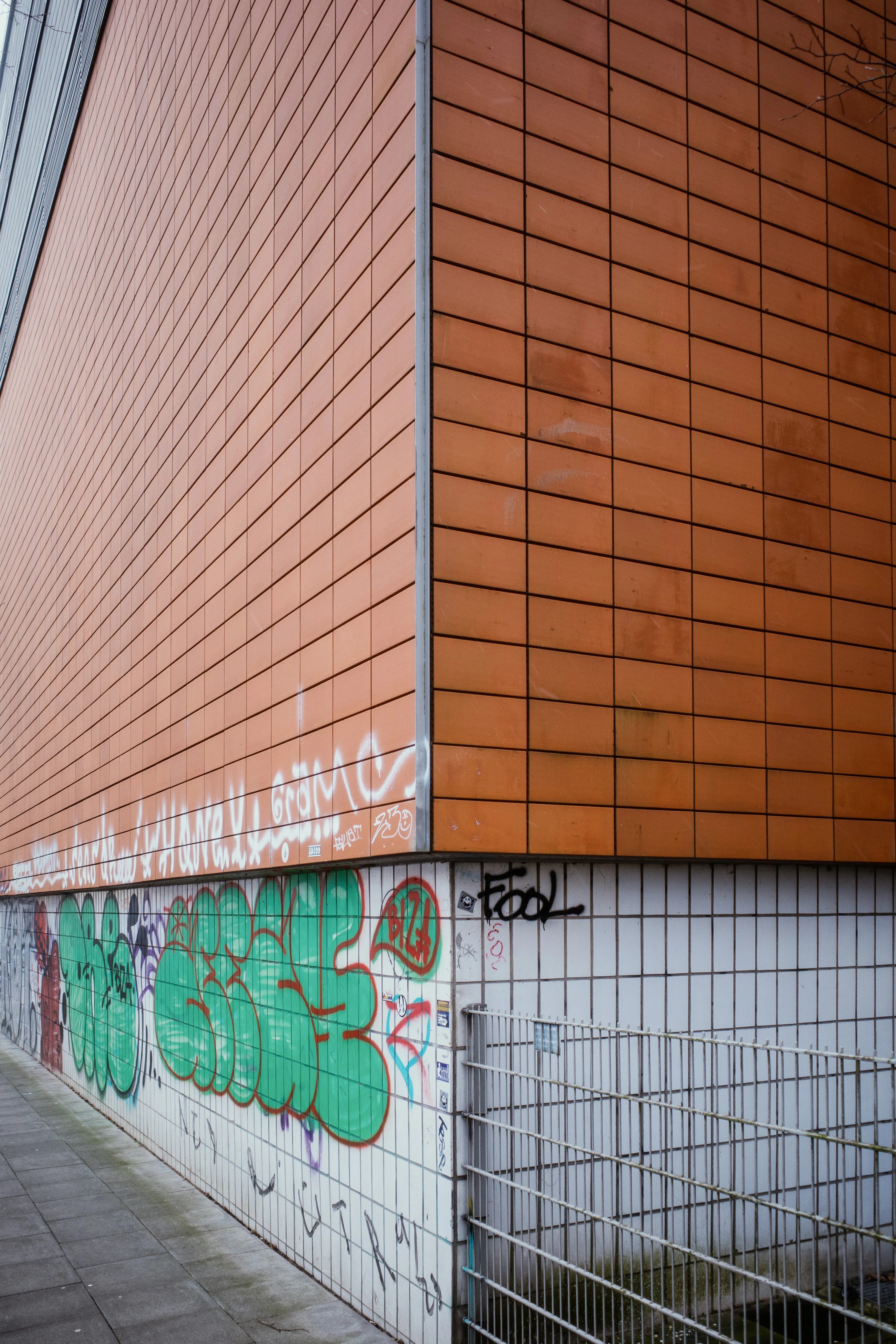 A building corner with orange tiles and graffiti on its lower walls.