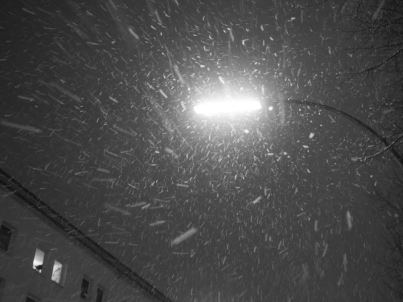 A streetlight illuminates falling snowflakes at night next to a building.