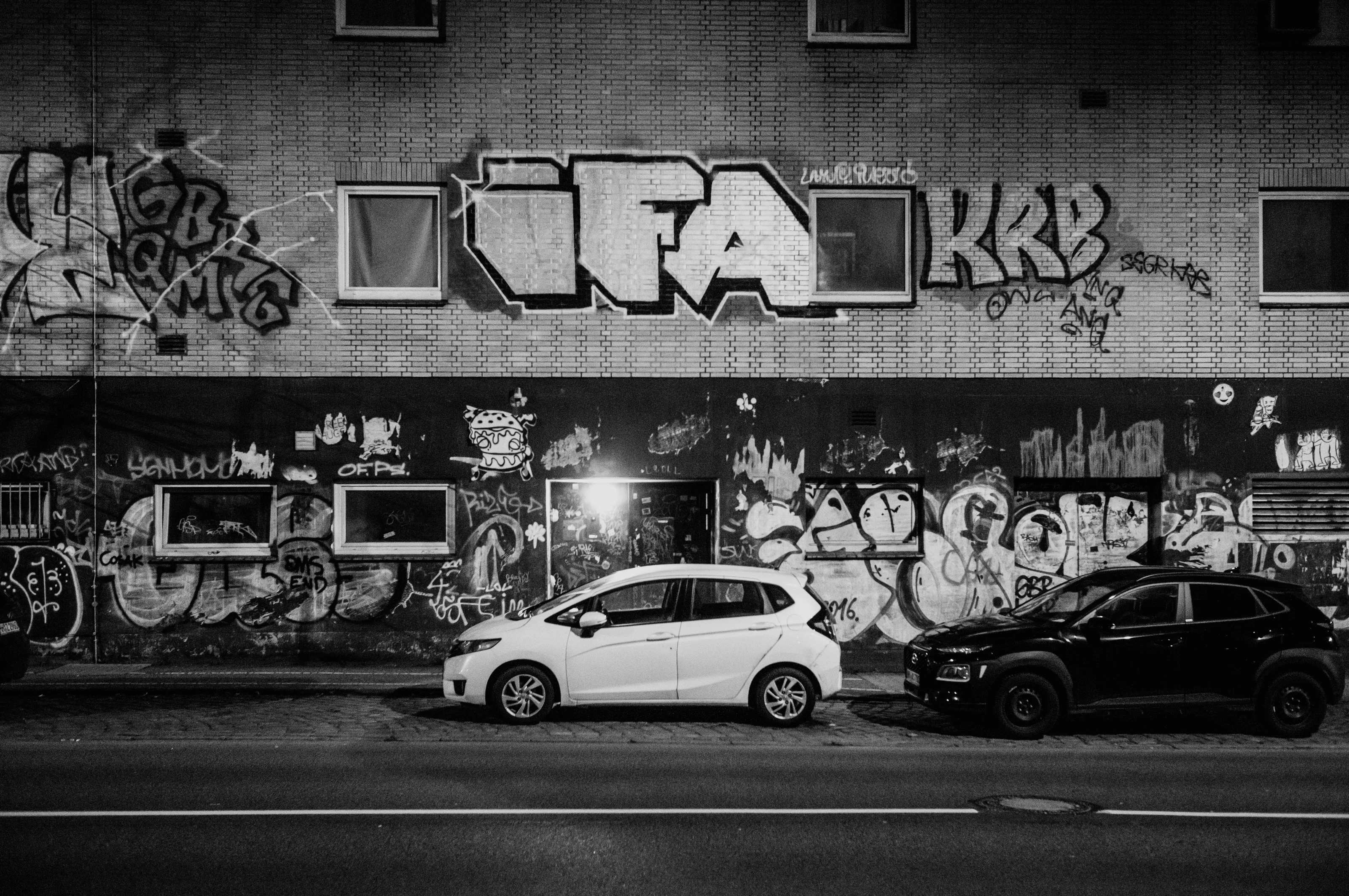 Two parked cars in front of a graffiti-covered building at night.
