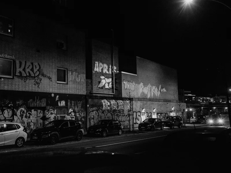 Nighttime street scene with graffiti-covered building and parked cars.