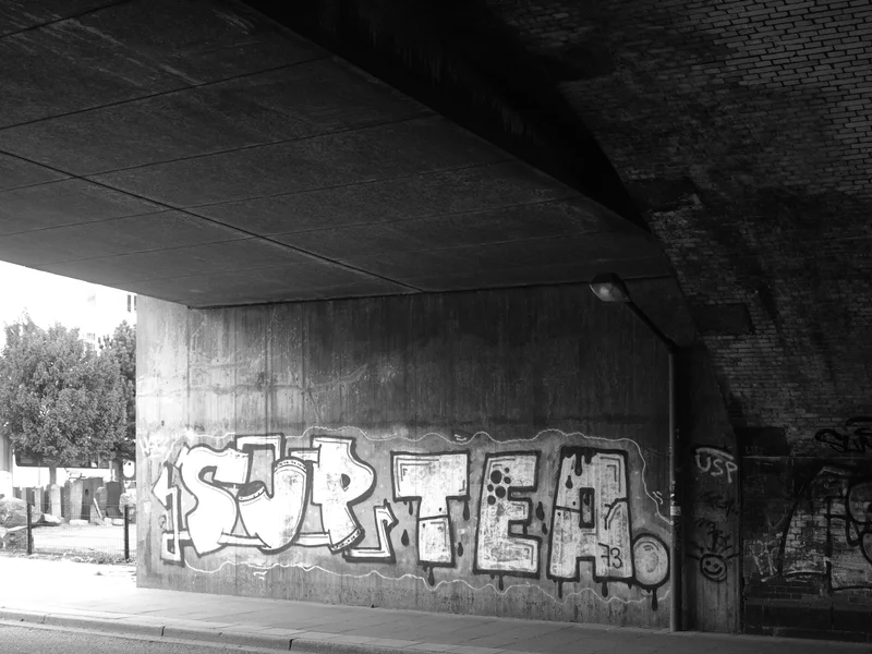 Black and white photo of graffiti under an overpass.