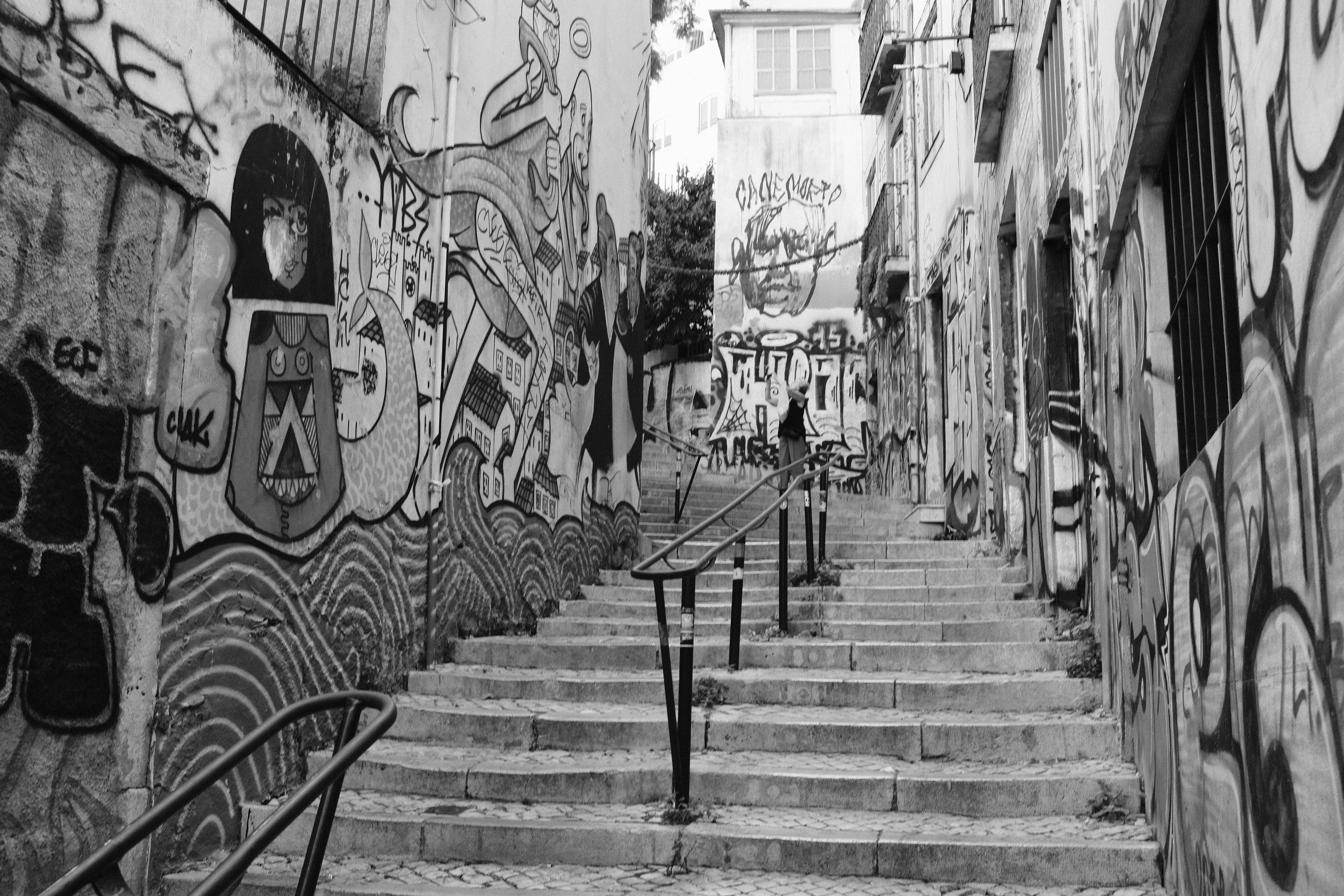 Black and white photograph of a narrow stairway lined with graffiti-covered walls.