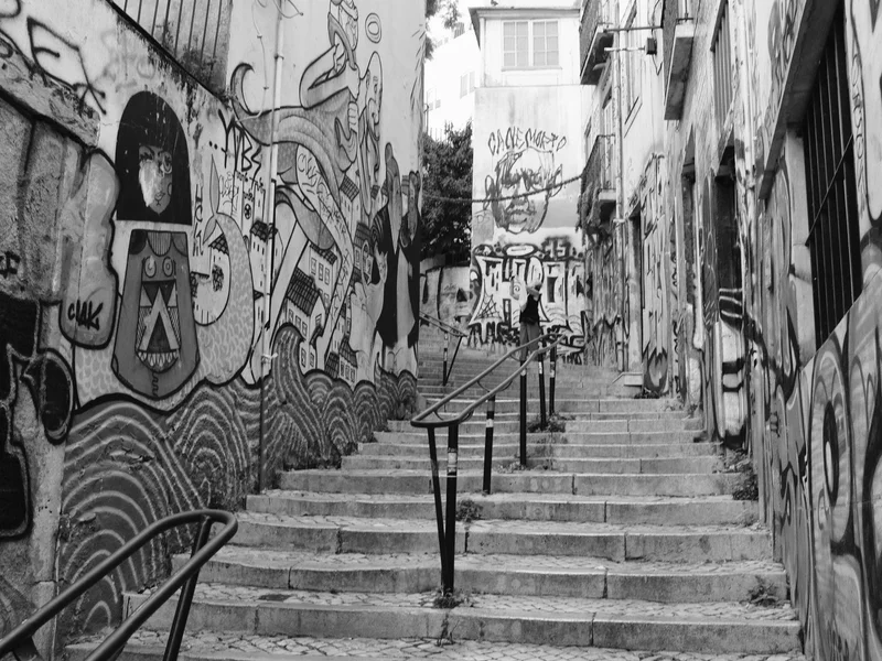 Black and white photograph of a narrow stairway lined with graffiti-covered walls.