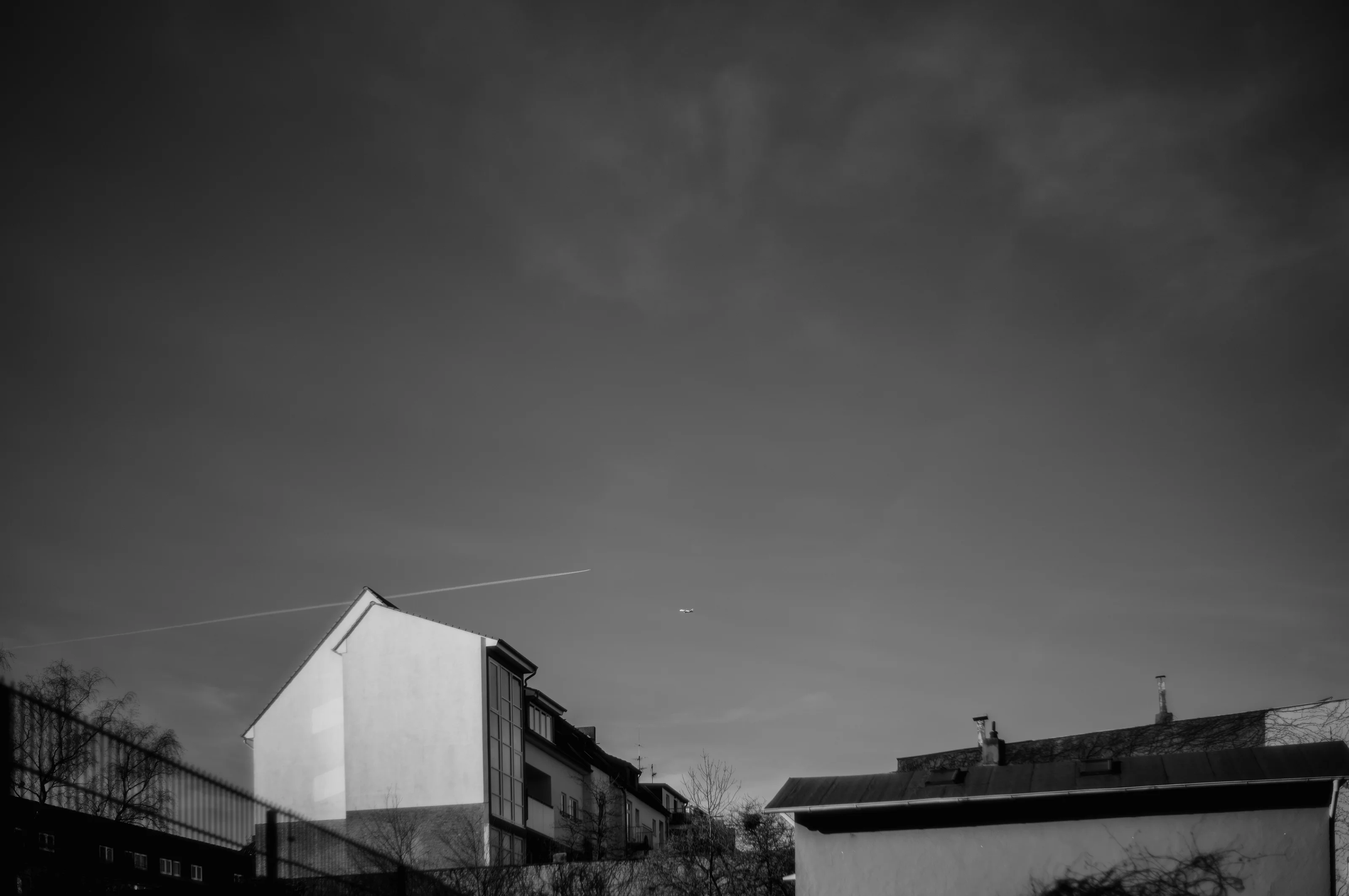 A minimalist cityscape with a contrail and small airplane above a building.