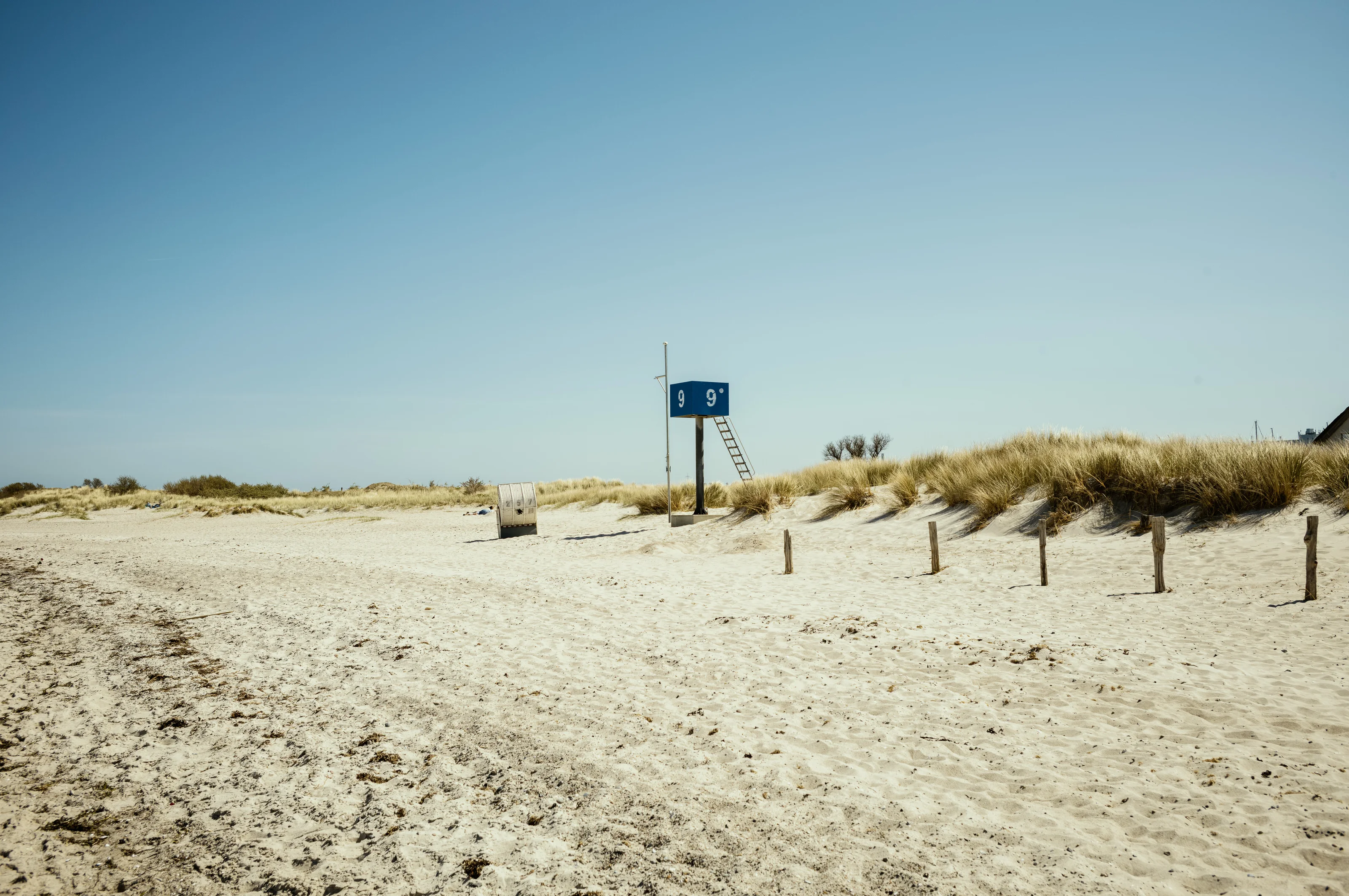 A sandy beach with a blue lifeguard station and grassy dunes in the background.