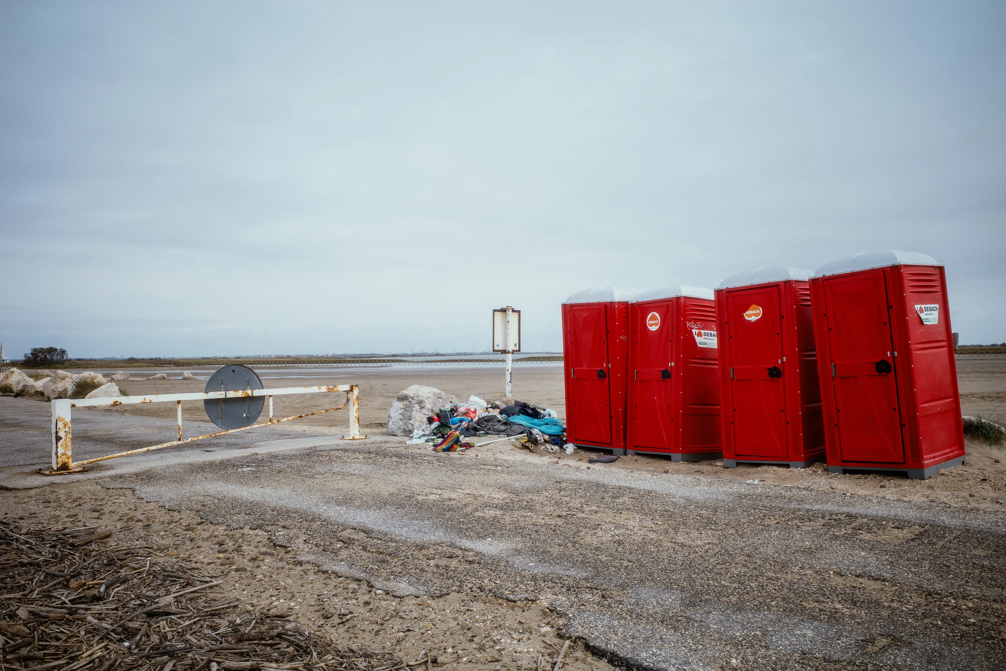 Red portable toilets next to a pile of trash on a deserted landscape.