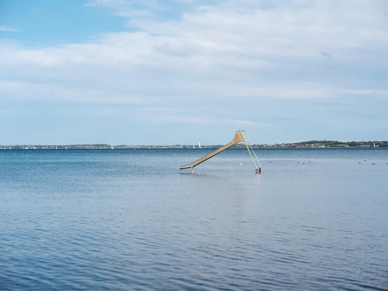 A water slide descending into a calm sea under a partly cloudy sky.