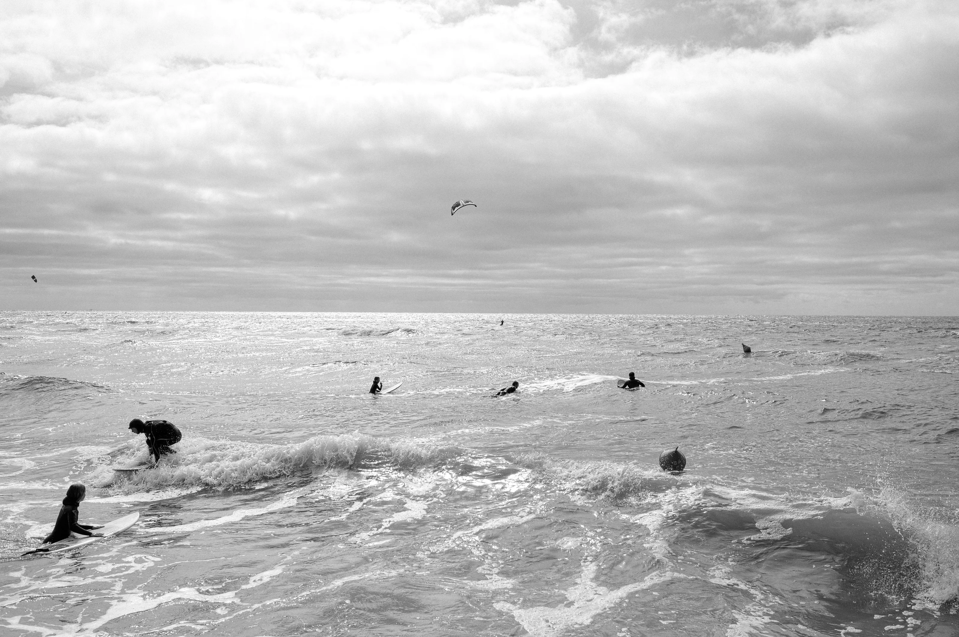Surfers in the ocean under a cloudy sky with a kite in the background.