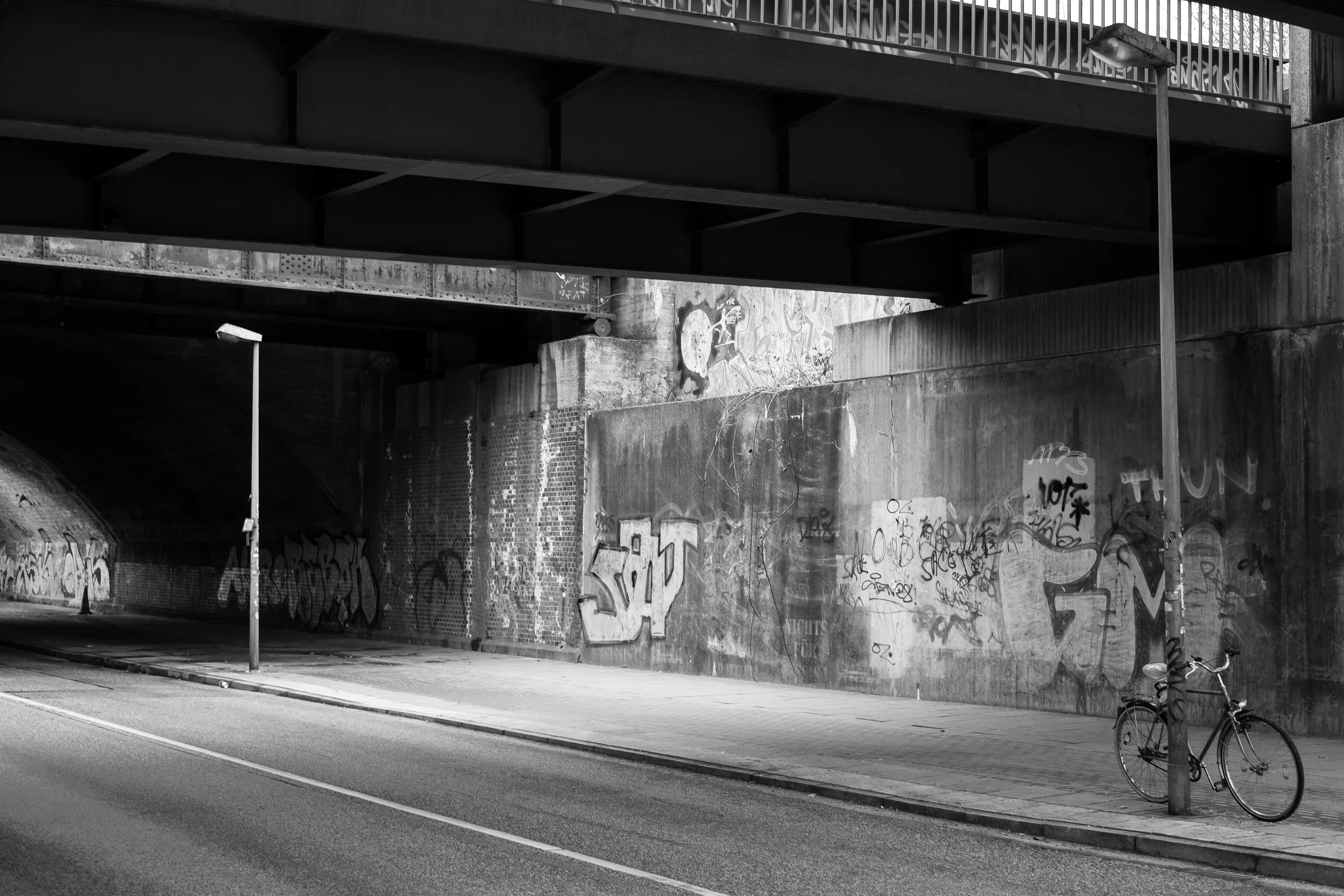 Black and white photo of a graffiti-covered underpass with a bicycle leaned against a lamp post.