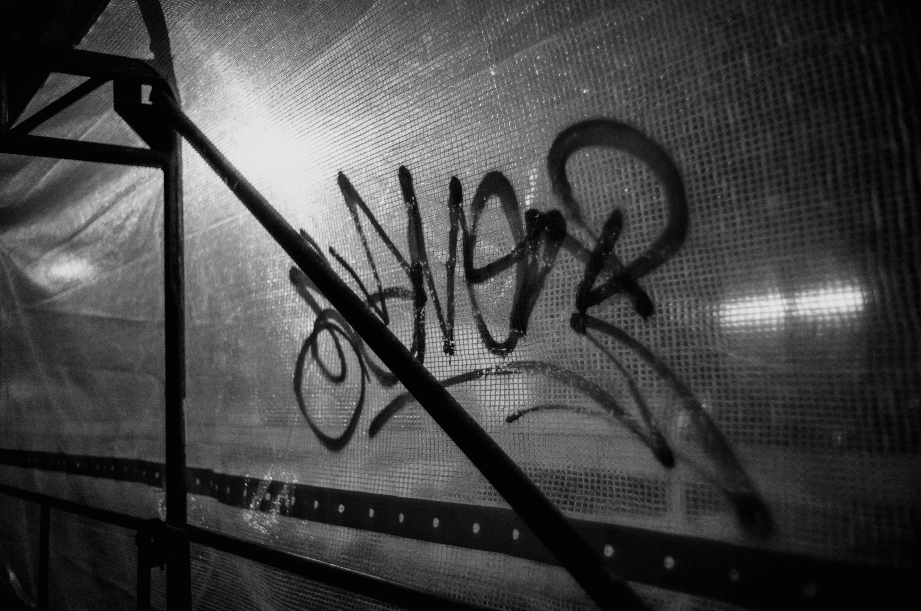 Black and white image of graffiti on a translucent surface with metal supports.
